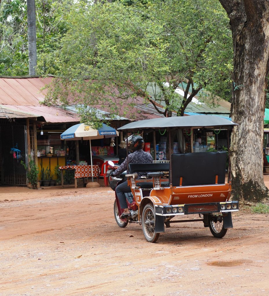 A tuk tuk driver on his ride. It says "From London" on the back of the Tuk Tuk.